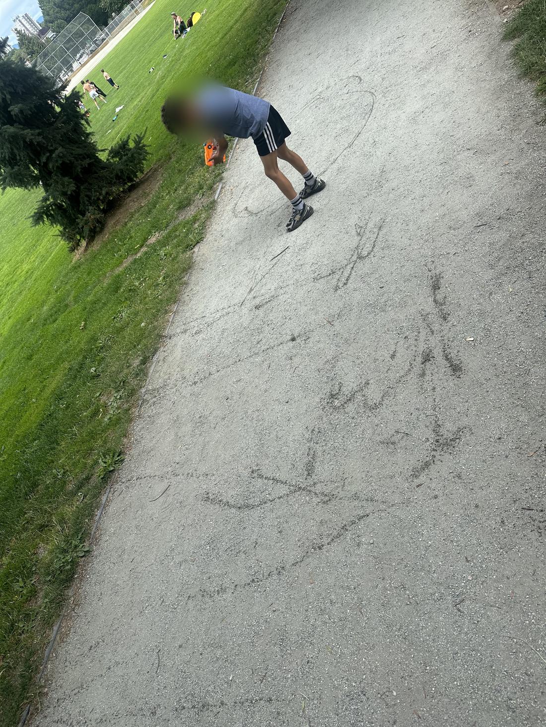 A child drawing with chalk on a path outdoors. Face is blurred.