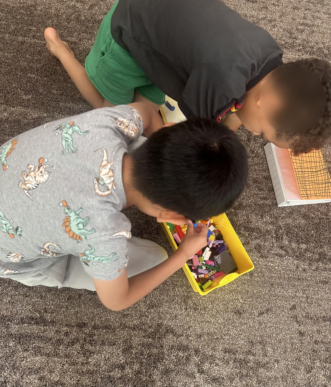 Two children building together with a bin of blocks. Face is blurred.