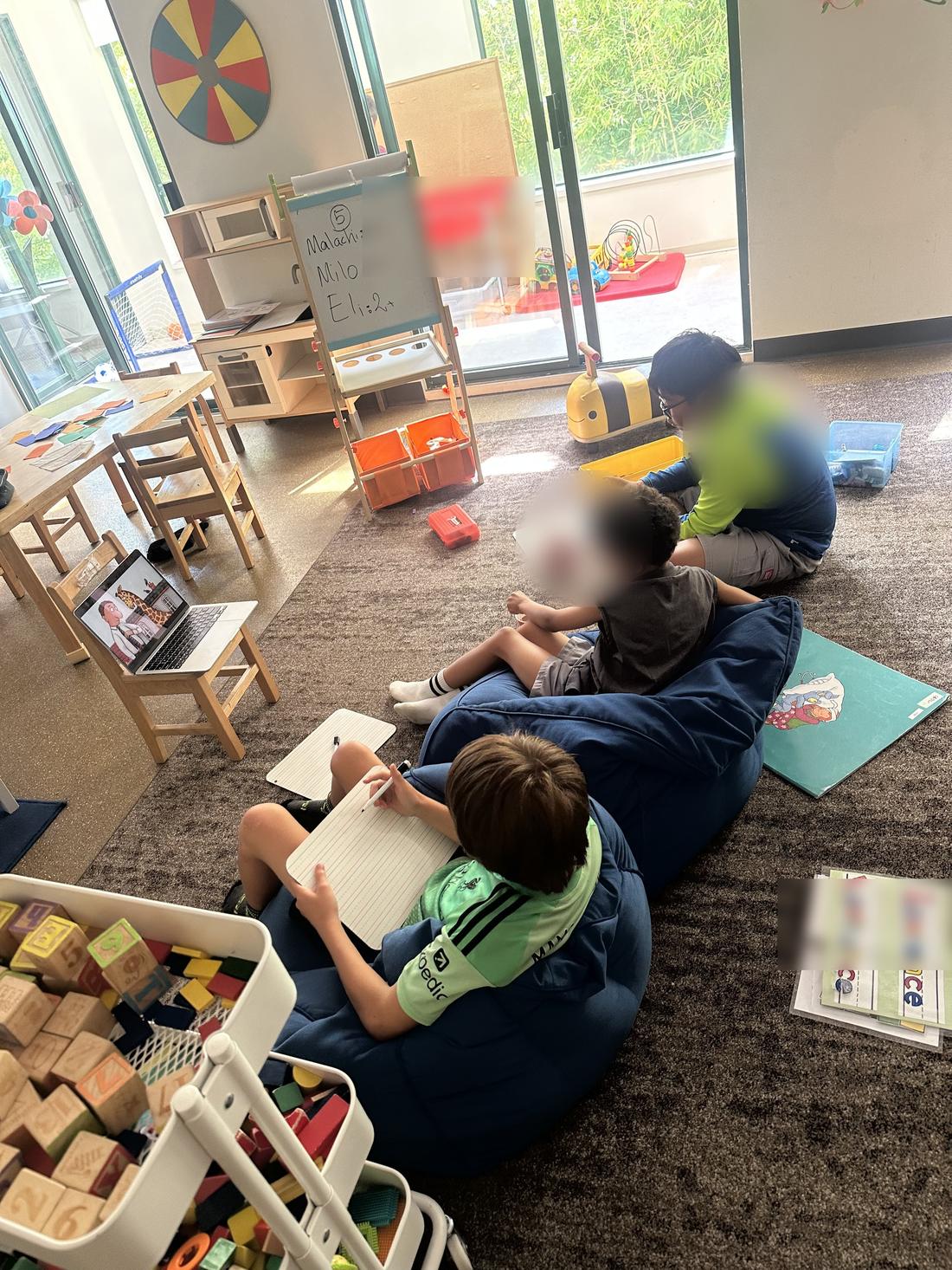Children reading and writing together on bean bags. Faces are blurred.