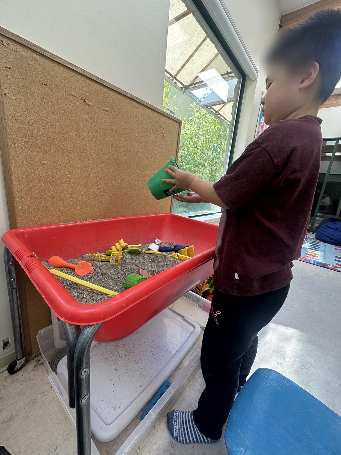 A child playing at a sensory sand table. Face is blurred.